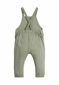 Salopette en coton vert avec des bretelles croisées et deux boutons à la taille, dotée de poignets retroussés aux chevilles et d'une coupe décontractée.