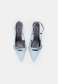 Babies à talons slingback bleu clair avec des bouts pointus, en cuir, deux boucles en argent ajustables sur les sangles, et une texture lisse.