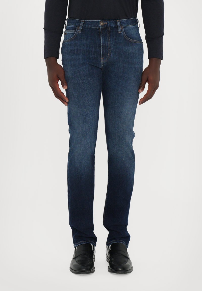 Σκούρα μπλε τζιν παντελόνα με σλιμ εφαρμογή, διαθέτει πέ�ντε τσέπες, διακριτές ραφές και κλασικό κούμπωμα με κουμπί στη μέση.
