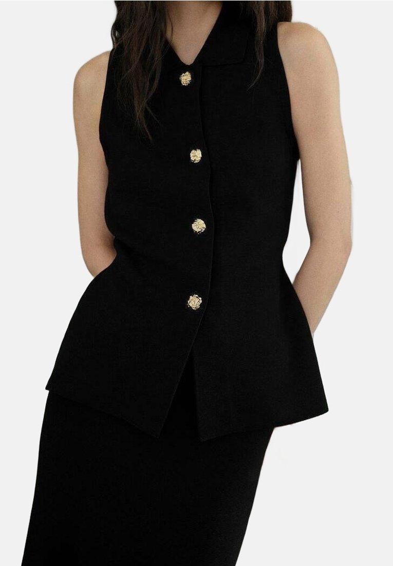 Femme portant un haut noir sans manches avec un col et quatre boutons dorés à l’avant, associé à une jupe noire.