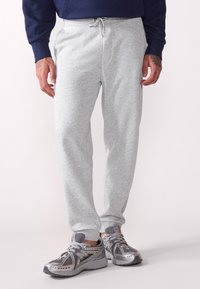 Graue Jogginghose mit weicher Textur, elastischem Bund und Kordelzugdetails. Kombiniert mit grauen Sportschuhen, die über Netz- und Gummielemente verfügen.