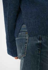 Námornícky modrý, textúrovaný vlnený sveter s vroubkovanými rukávmi, v kombinácii so svetlomodrými džínsy s klasickým dizajnom piatich vreciek.