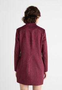 Bordeauxfarbener Kunstwildledermantel mit sleekem Design, langen Ärmeln und hohem Kragen. Verfügt über eine zentrale Naht, die entlang des Rückens verläuft.