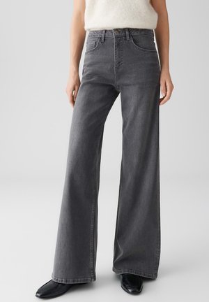 Jean large gris en denim avec une texture lisse. Présente un design classique avec cinq poches et des détails cousus le long des coutures.
