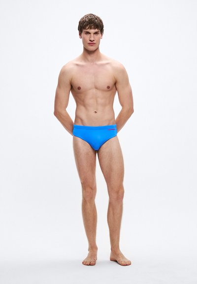 Μπλε ανδρικά μαγιό με λεία υφή, που διαθέτουν αντίθετη μέση και λεπτομέρεια με λογότυπο. Ο σχεδιασμός είναι χαμηλόμεσος και εφαρμοστός.