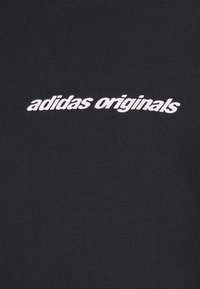 Tela negra con textura acanalada que presenta el logo de "adidas originals" en blanco, centrado y bordado en el pecho.