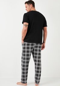 T-shirt di cotone nera abbinata a pantaloni a quadri bianco e nero. L'outfit presenta una vita elastica e una vestibilità rilassata.