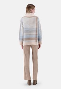 Übergroßer Pullover im hellblauen und beigen Karomuster, mit geripptem Kragen und Saum; kombiniert mit beigen Hosen und Schuhen mit Blockabsatz.