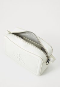 Borsa rettangolare in pelle bianca con chiusura a zip, logo 'CK' impresso e hardware in argento. L'interno presenta una morbida fodera e pochi scomparti.