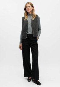Grå fleecevest med knapper, parret med en lys grå turtleneck, sorte stribede bukser og sorte sko. Teksturstof og skræddersyet pasform.
