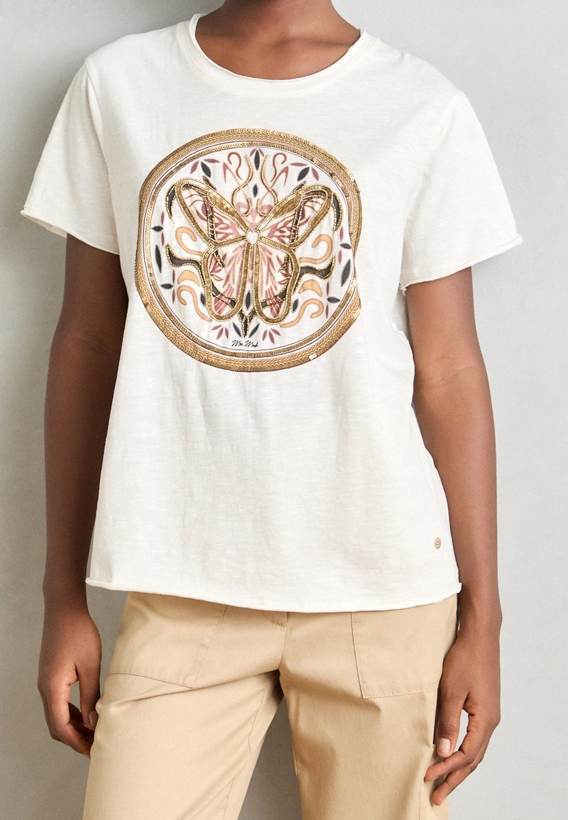 Bílá tričko s krátkým rukávem s kruhovým designem motýla ve zlatých a růžových akcentem, vyrobené z měkké, texturované látky.