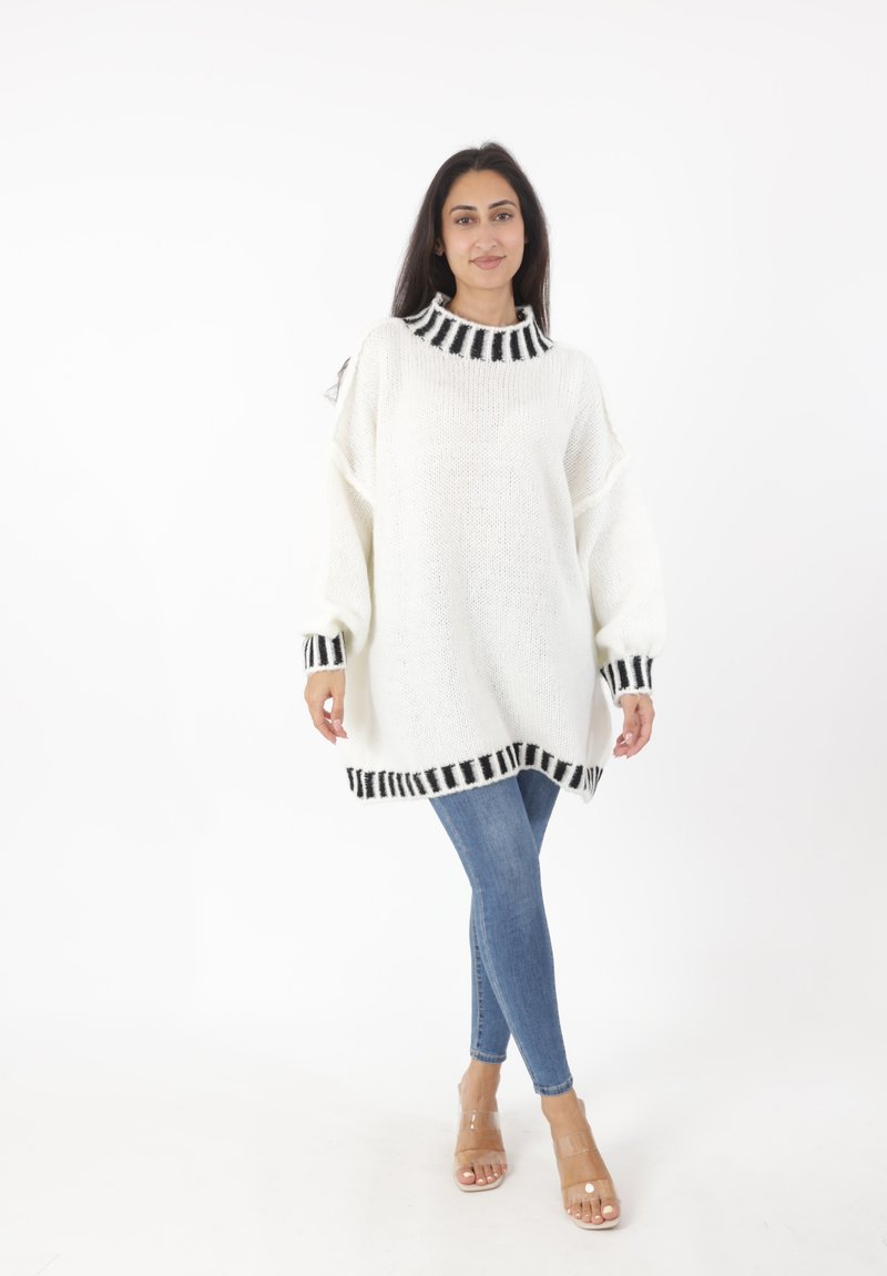 Hvid strikket sweater med sorte stribede detaljer ved halskanten og kanten, parret med blå skinny jeans og sandaler med gennemsigtige stropper.