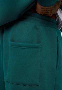 Teal katoenen joggers met een rechthoekige patch pocket op de dij, een gladde textuur en een elastische tailleband.