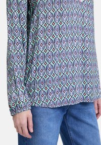 Langärmliges Shirt aus gemustertem Stoff mit geometrischen Formen in Blau, Pink und Grün. Figurbetonte Manschetten mit elastischem, leichtem Material.