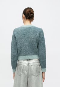 Απαλό πετρόλ πουλόβερ με βαθμιαία αποχρωματισμένη κάτω άκρη και μακριά μανίκια, σε συνδυασμό με λαμπερό ασημί παντελόνι με φαρδιά πόδια. Πλάγια όψη από πίσω, με ελάχιστες λεπτομέρειες.