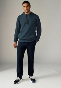 Sudadera de textura azul oscura con cordón, combinada con pantalones oscuros y zapatillas navy. La sudadera tiene un corte relajado y un patrón sutil.