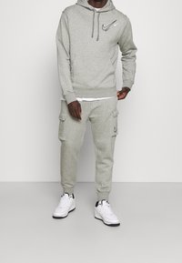 Grijze katoenen hoodie met een voorzak en trekkoord. Gecombineerd met bijpassende cargobroek met zijzakken. Witte sneakers.