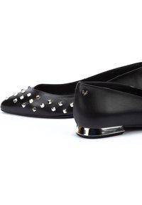 Bailarinas de cuero negro con tachuelas plateadas en la puntera y un pequeño acento de tacón metálico. Textura suave con un diseño elegante.