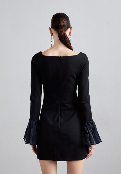 Black dress with long sleeves and sheer ruffled cuffs. Square neckline, fitted silhouette, and a discreet back zipper detail.