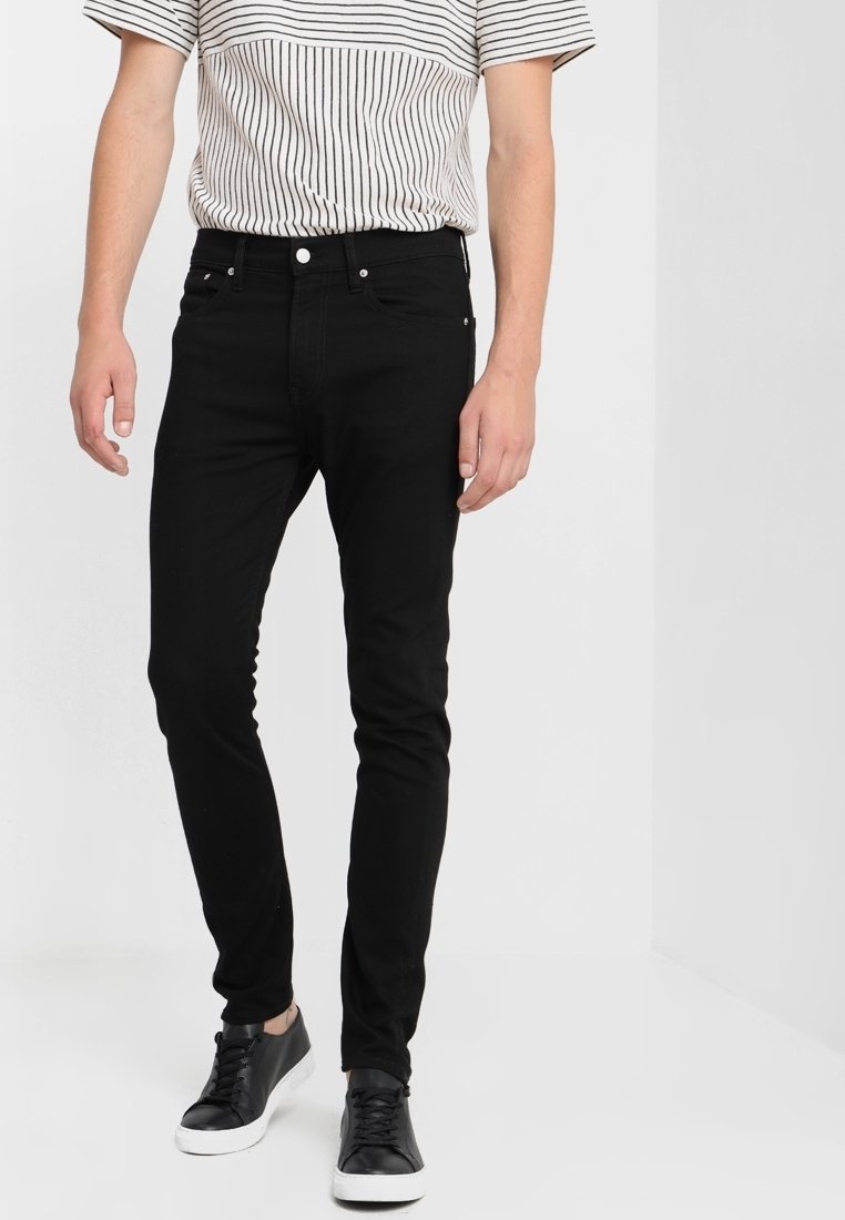 Svarta slim-fit jeans i denim med fem fickor, dragkedja och silverfärgad hardware. Kombinerat med en randig t-shirt och svarta sneakers.