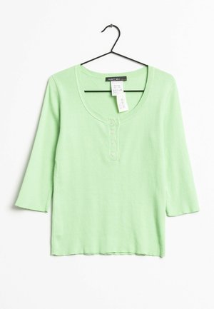 Zielona, prążkowana bluzka z długim rękawem, z dekoltem w serek, guzikami z przodu i rękawami ¾. Tkanina wydaje się miękka, wisi na czarnym wieszaku.