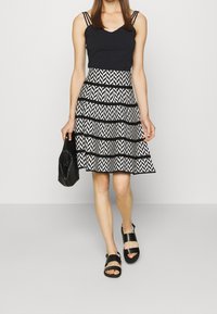Top nero senza maniche con doppie spalline, abbinato a una gonna fluida di lunghezza al ginocchio con un motivo a zigzag bianco e nero. Accessori neri completano il look.