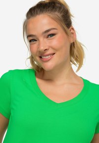 Zielona bawełniana koszulka z dekoltem w serek i krótkimi rękawami. Materiał wydaje się gładki, a fason jest dopasowany.