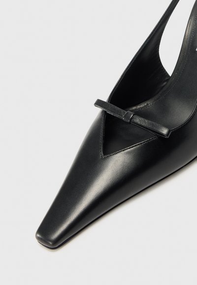 Črne usnjene čevlje s koničasto obliko in izrezljanim dizajnom, ki vključujejo majhen lok na zgornjem delu in elegantno, gladko teksturo.