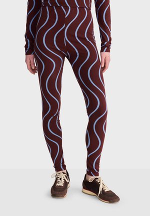 Leggings avec une base marron et des rayures verticales ondulées bleu clair, portés avec des baskets marron à lacets blancs.