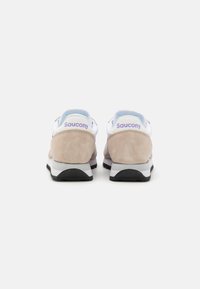 Bež antilop i bijele mrežaste tenisice s crnom potplatom. "Saucony" logo u svijetlo ljubičastoj boji na peti. Standardni dizajn s vezicama.