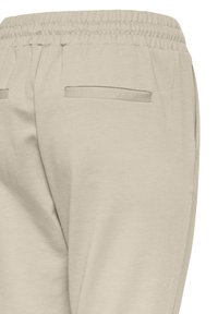 Pantalon beige à taille élastique avec deux poches passepoilées à l'arrière, confectionné dans un tissu doux et légèrement texturé.