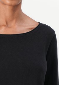 Black long-sleeve shirt with a wide neckline, made of soft, textured fabric; features a simple, clean design and fitted silhouette.