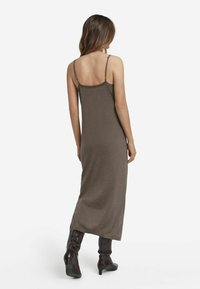 Brun ärmlös klänning, knälång, figurnära silhuett, slät textur, minimal detaljering. Bärs med mörka knähöga stövlar.