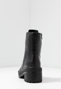 Zwarte enkellaars van imitatieleren met krokodillenstructuur, een ronde neus en een robuuste zool. Voorzien van een zijrits voor makkelijk aan- en uittrekken.