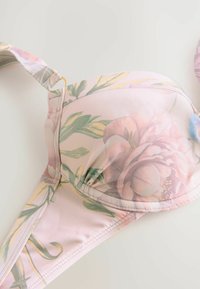 Beha met bloemenpatroon in zachtroze stof, met voorgemoulde cups, verstelbare banden en gouden accenten. Over het geheel een gladde textuur.