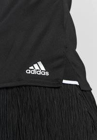 Svart träningslinne med texturerad franskant, med en vit Adidas-logotyp på vänster sida. Tillverkat av lätt och elastiskt material.