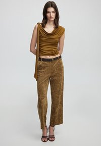 Top drapeado color canela con escote en cowl, combinado con pantalones sueltos de textura en un tono similar y sandalias marrones con tiras.