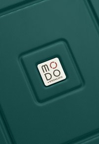 Surface texturée de valise verte avec un logo de marque carré blanc indiquant « MODO by Roncato » au centre.