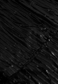 Schwarzer Paillettenstoff mit einem strukturierten Muster aus horizontalen Linien und kreisförmigen Pailletten auf der Oberfläche, das einen geschichteten Effekt erzeugt.