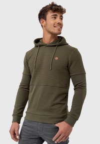 Olijfgroene hoodie met quilted textuur op de borst, trekkoordkap en ribgebreide zoom. Heeft een klein leren logopatch.