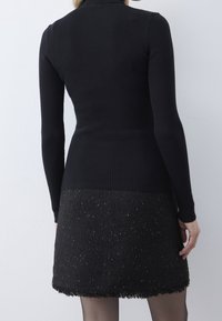 Gestreiftes schwarzes Langarmoberteil, kombiniert mit einem glitzernden schwarzen Minirock mit fransigem Saum. Der Stoff zeigt auf subtile Weise goldene Flecken.