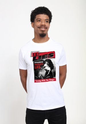Mann mit lockigem Haar und Bart, der ein weißes T-Shirt mit rotem und schwarzem Aufdruck mit dem Schriftzug „"GN'R LIES Exclusive Reckless Life Living With The Danger"“ trägt.