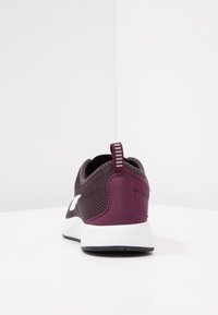 Musta ja viininpunainen urheilukenkä, jossa verkkokuvioitu päällinen, valkoinen välipohja ja kuvioitu kantapään vetokiristin. Varustettu vetolenkillä ja sivussa hillityllä brändäyksellä.