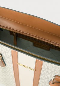 Μπεζ και καμηλό τσάντα με υφασμάτινο μοτίβο, χρυσά μεταλλικά στοιχεία, εσωτερική τσέπη με φερμουάρ και δερμάτινες ρίγες. Ορατό λογότυπο στο εσωτερικό.