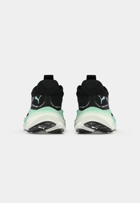 Baskets de sport noires avec une semelle intermédiaire vert menthe, des tiges texturées et une semelle extérieure en caoutchouc noir. Présente une languette au talon et un détail de logo.