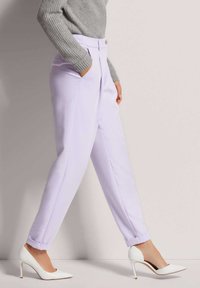 Lilac tailored trousers with a flat front, side pockets, and cuffs, paired with white high-heeled shoes and a grey ribbed sweater.