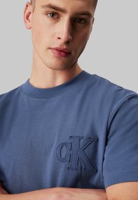T-shirt in cotone blu navy con un logo 'cK' ricamato e testurizzato sul lato sinistro del petto, scollatura rotonda e maniche corte. Tessuto con una superficie liscia.