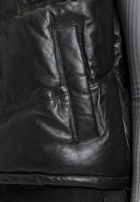 Schwarze Lederjacke mit strukturierter Oberfläche, einer Seitentasche und dezenten Nähten, die vorne sichtbar sind.