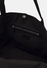 Czarna torebka na ramię wewnątrz z kieszonką na zamek i skórzaną naszywką. Materiał jest gładki o matowym wykończeniu, z solidnymi uchwytami.