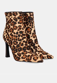 Par de botas de tobillo con estampado de leopardo, con punta afilada y altos tacones delgados negros, sobre fondo blanco.